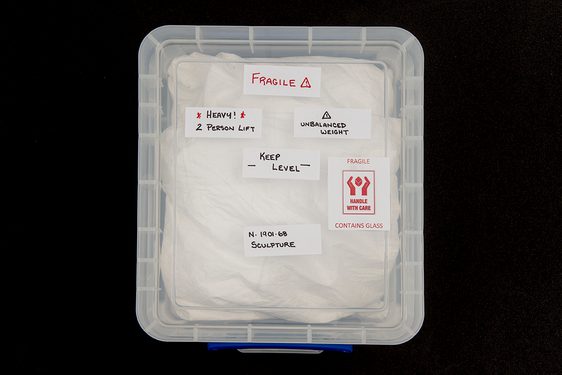 A plastic storage container with sticky labels reading, 'Fragile'. Inside the container is white packing material.